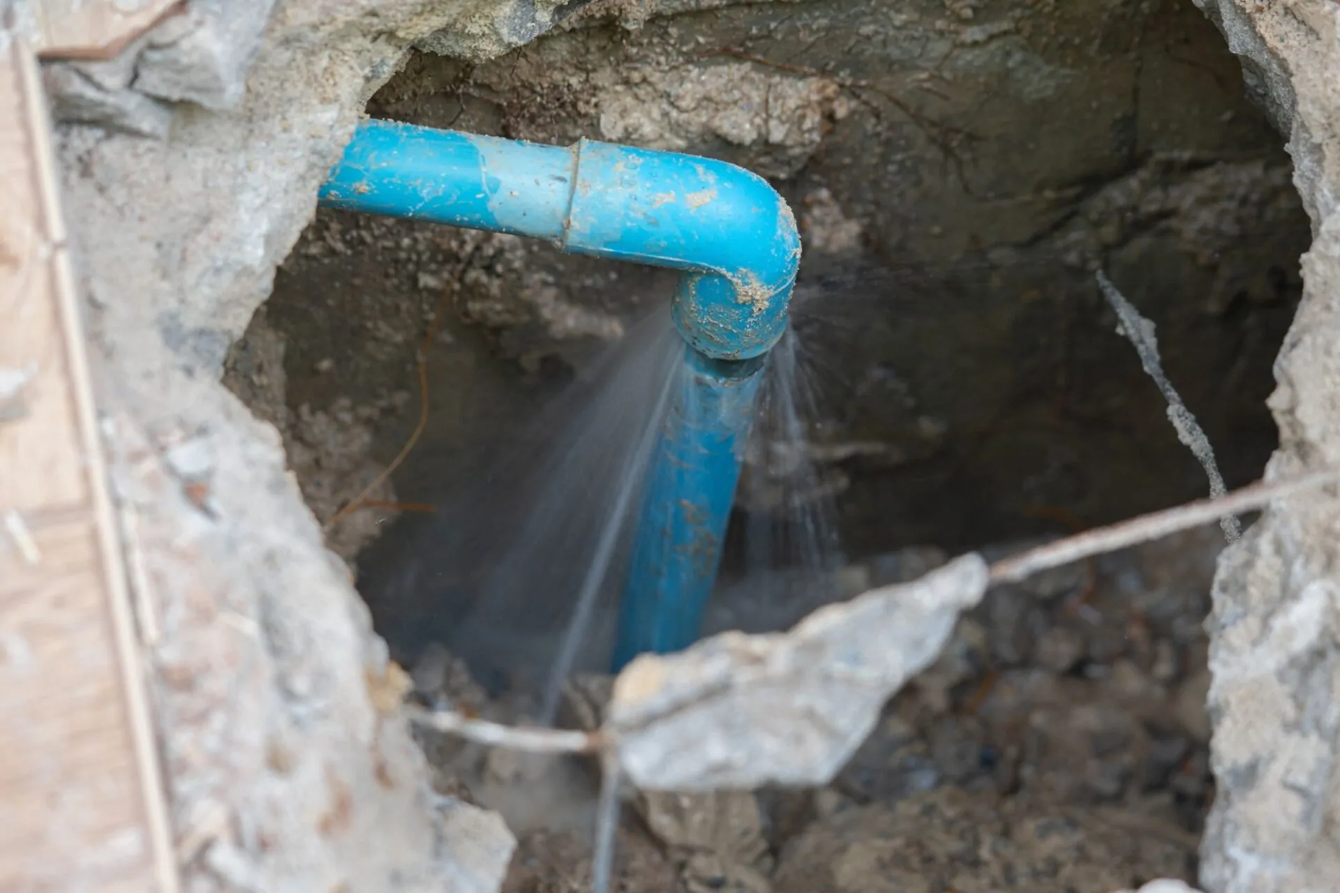 Leaking water from a blue underground pipe showing what causes plumbing leaks.