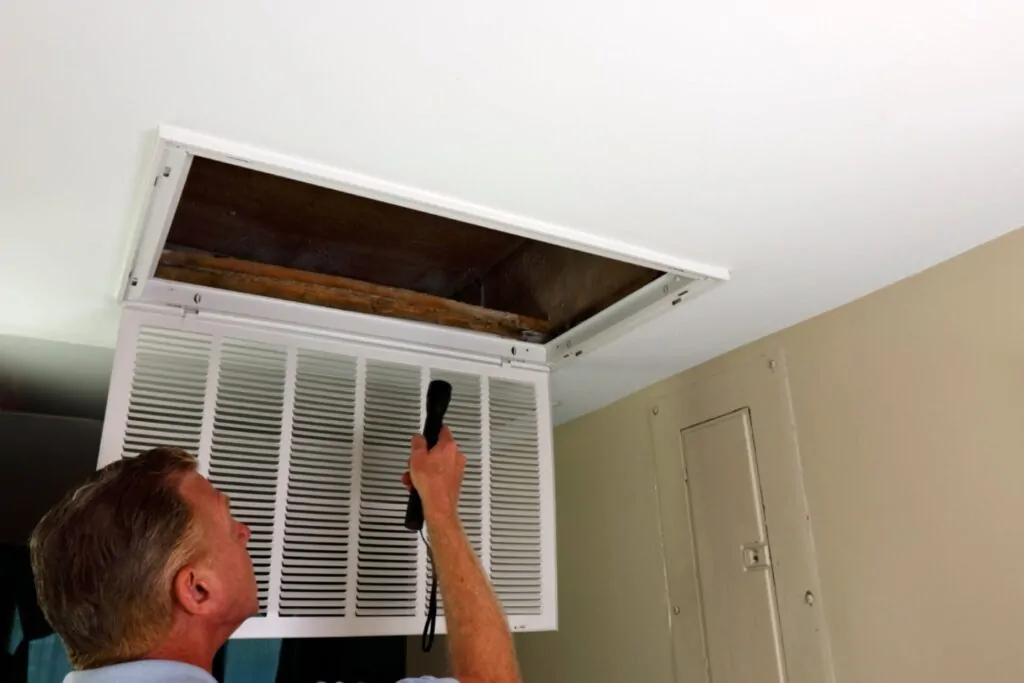 Air duct inspections showing an adult man shining a flashlight into an HVAC intake vent in a home entry to check airflow and duct condition