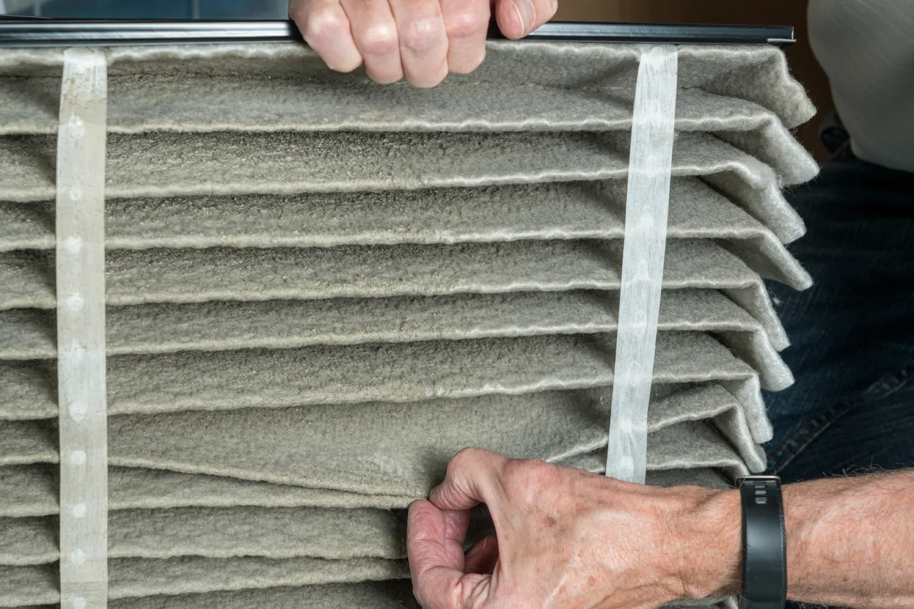 Technician removing a heavily soiled air filter during year-round HVAC maintenance in a Phoenix home.