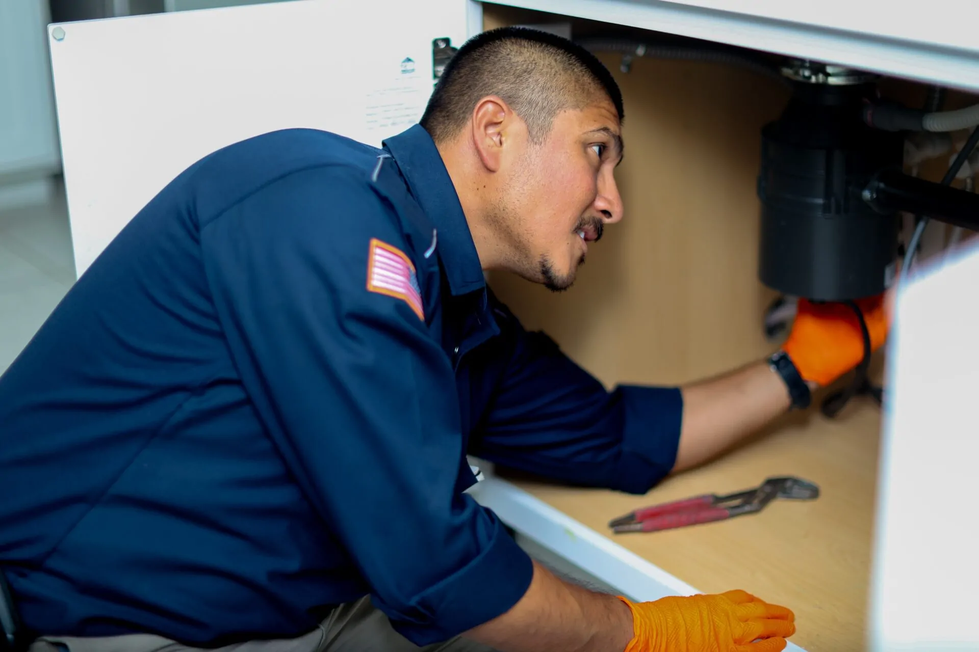 Canilu Air technician inspecting under-sink plumbing during summer plumbing repairs in AZ